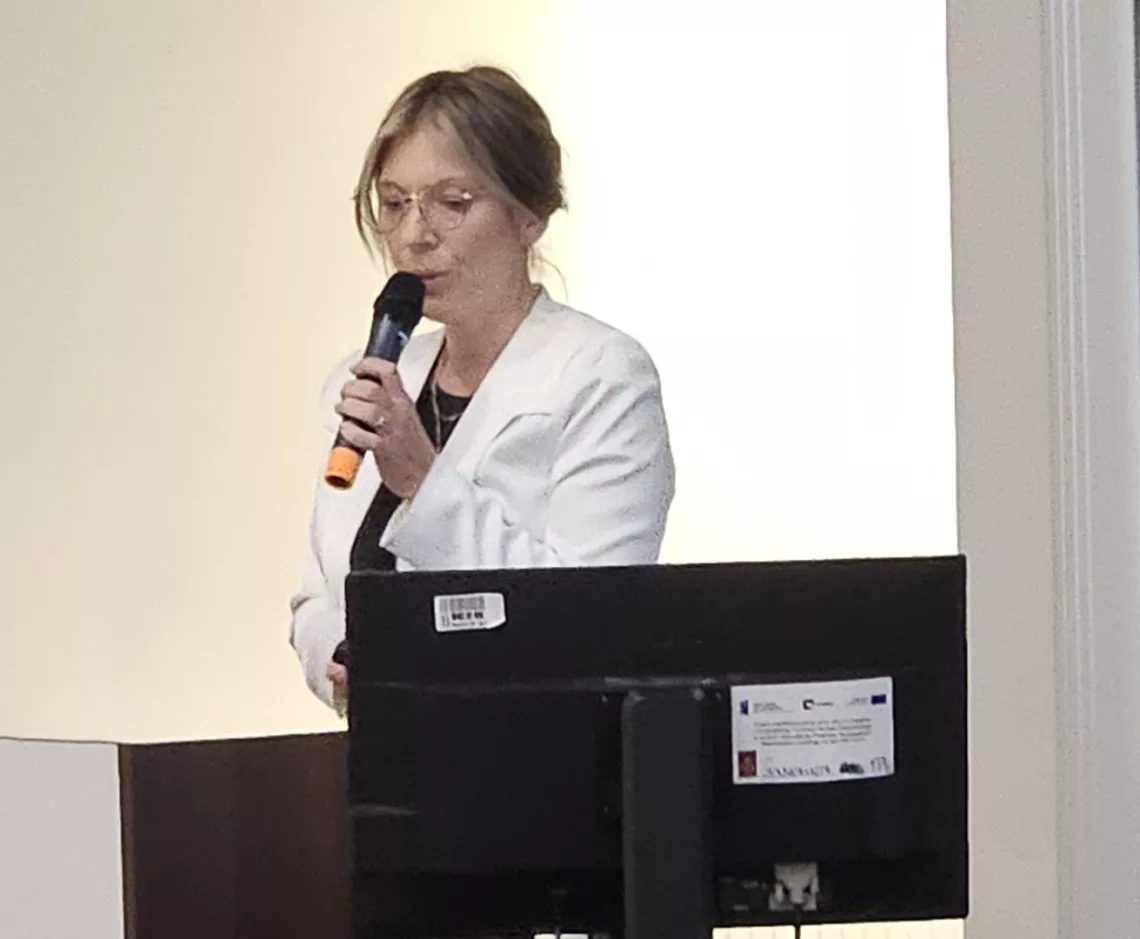 Przemawia wykładowczyni, trzymając mikrofon w ręku