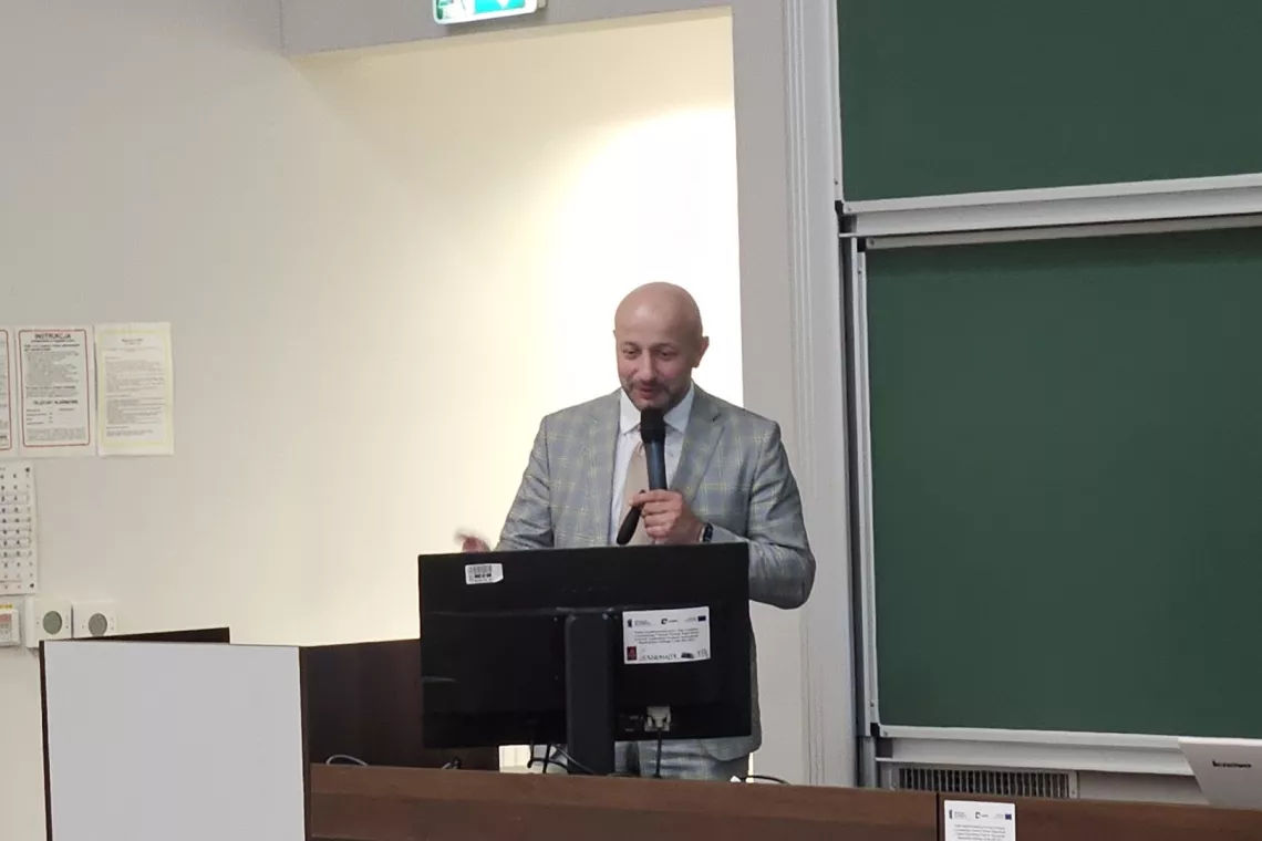 Przemawia wykładowca, trzymając mikrofon w ręku