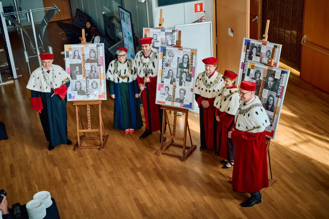 Rektorzy w togach stoją przy plakatach wystawy "Inspirujace kobiety, które wybrały łódzkie uczelnie"