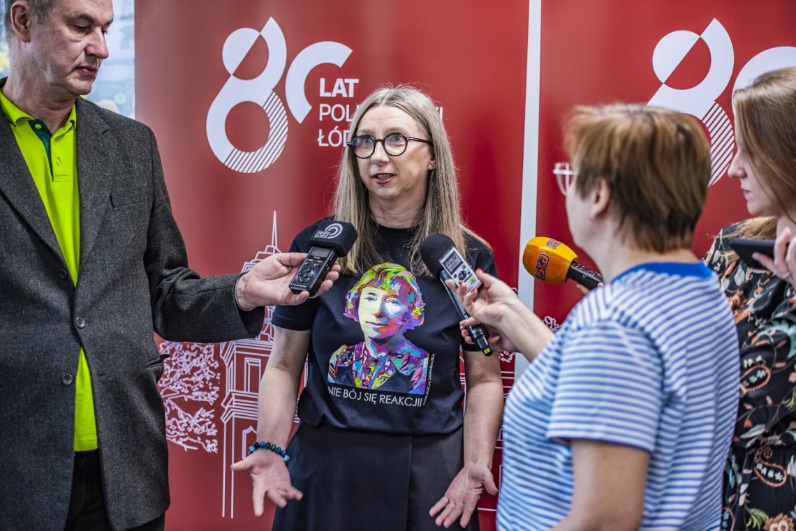 Kobieta udziela wywiadu mediom. W tle banery z napisem 80 lat Politechniki Łódzkiej