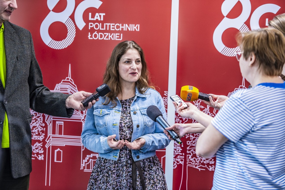 Kobieta udziela wywiadu mediom. W tle banery z napisem 80 lat Politechniki Łódzkiej