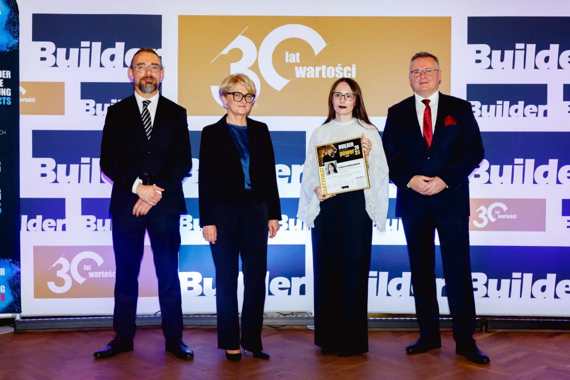 Cztery osoby, w tym jedna z dyplomem w ręku, stoją na tle kolorowej ścianki promocyjnej