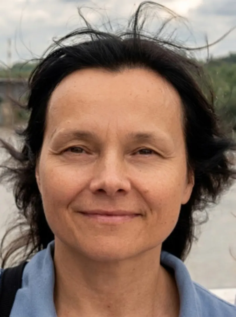 Twarz kobiety uśmiechniętej, ciemne rozwiane włosy, w tle krajobraz naturalny
