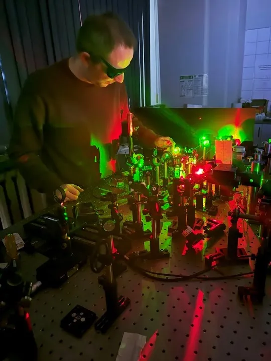 Mężczyzna w okularach ochronnych obserwuje wiązki laserowe przebiegające przez urządzenie znajdujące się na stole