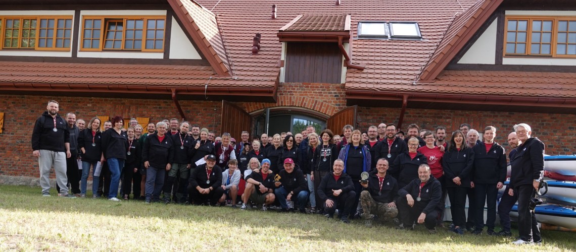Liczna grupa osób stoi przed budynkiem z cegły z czerwona dachówką