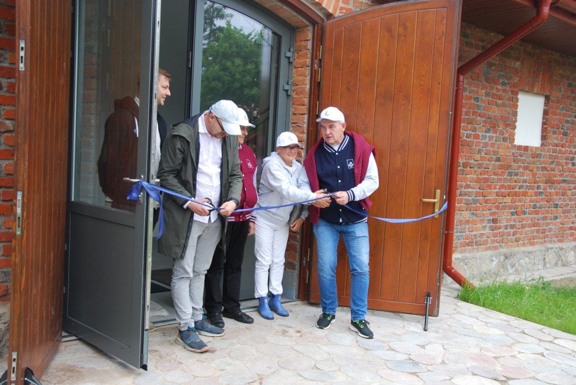 Pięć osób przecina wstęgę rozwieszoną w drzwiach budynku