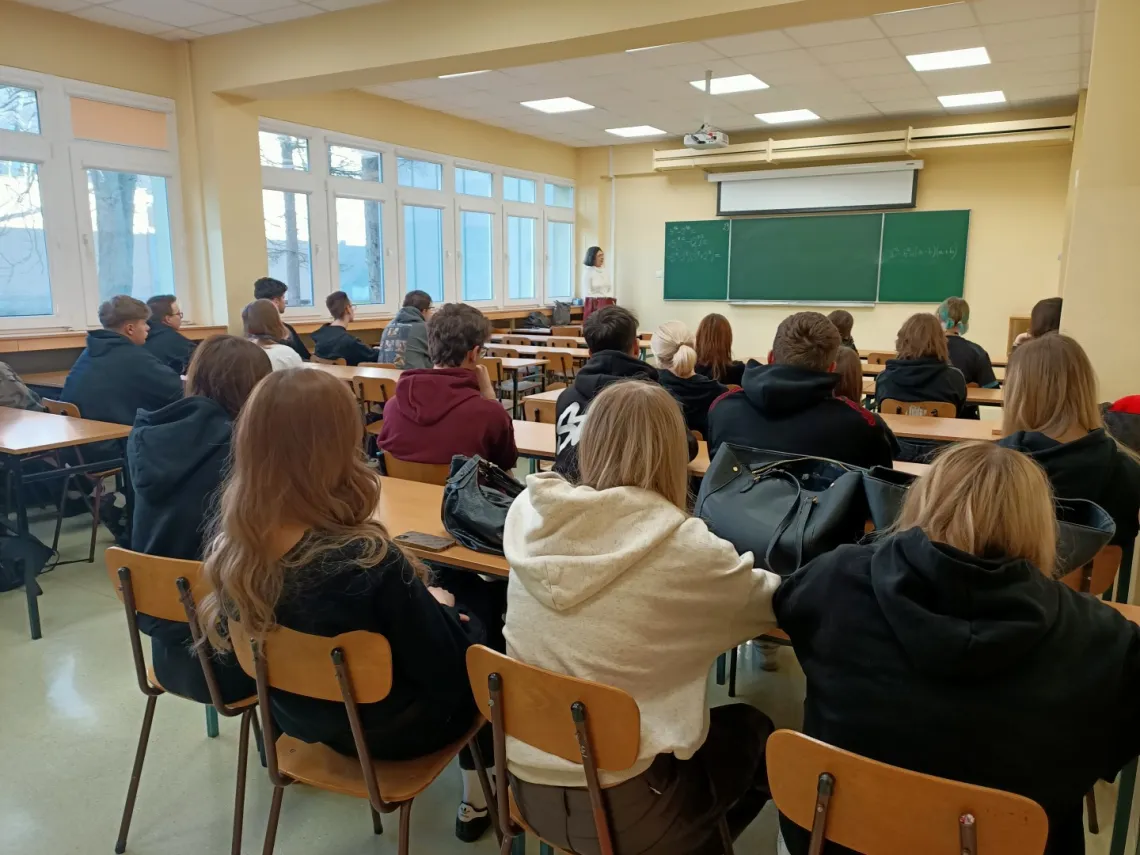 Uczniowie siedzą w ławkach sali ćwiczeniowej, słuchając wykładowcy stojącego przy tablicy