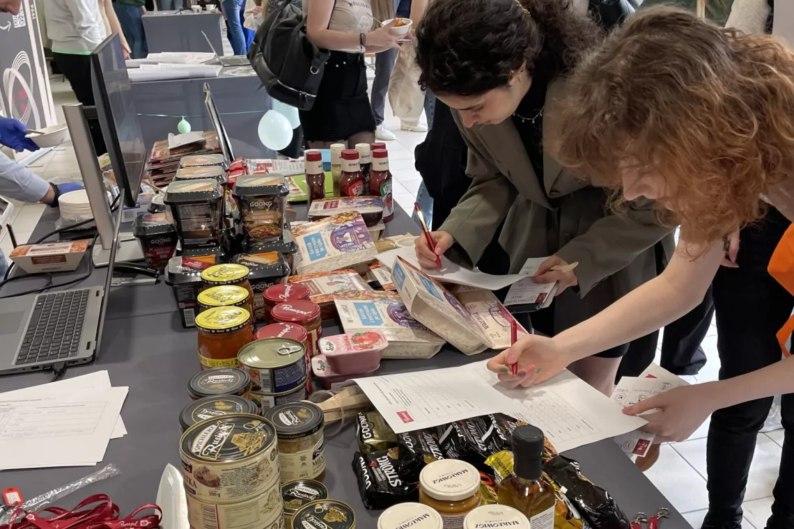 Grupa osób wypełnia formularze przy stole zastawionym róznymi produktami w słoikach