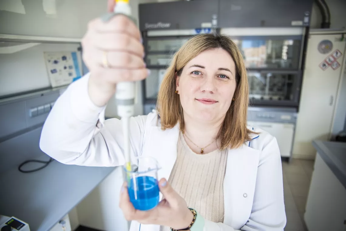 Badaczka w laboratorium trzyma w dłoniach szklane naczynie i przyrząd pomiarowy