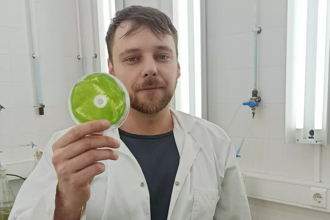 Młody naukowiec w białym fartuchu pokazuje próbkę