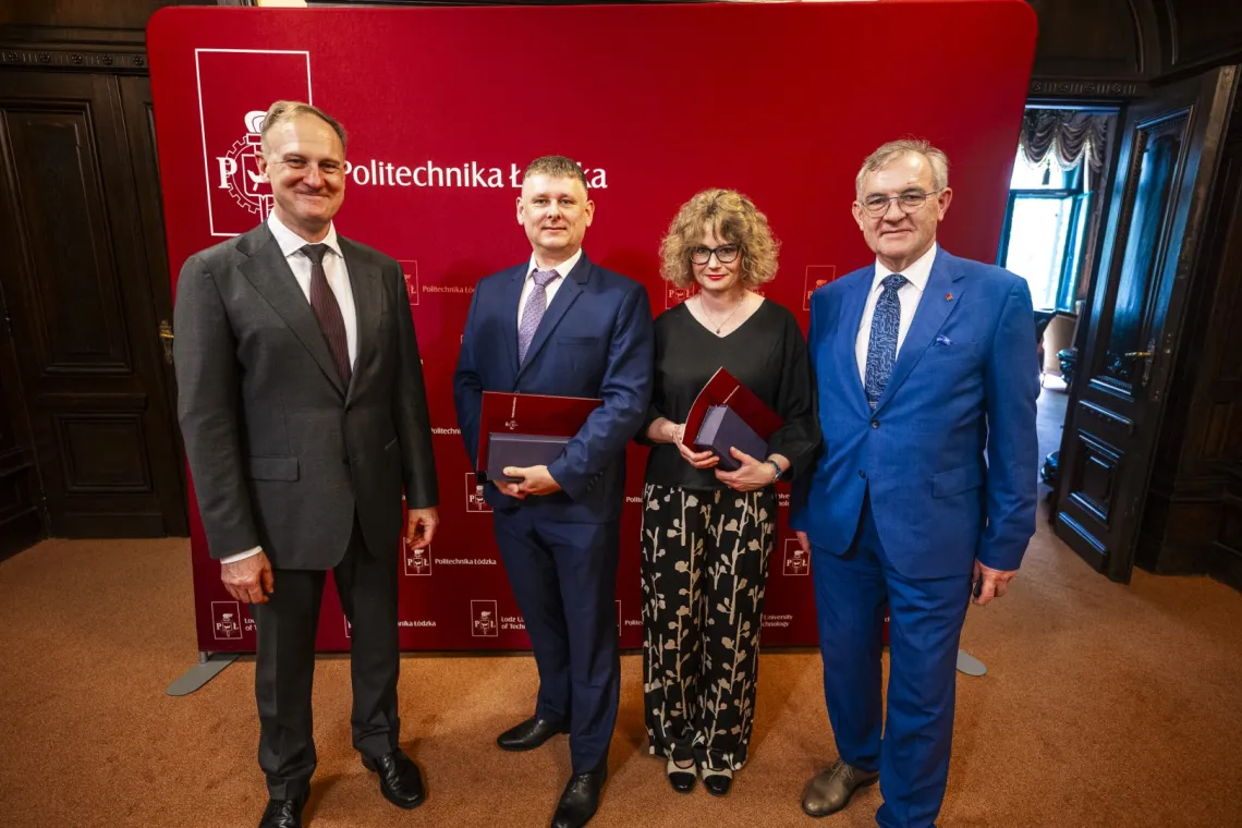 Kobieta w okularach i trzech mężczyzn pozuje do zdjęcia na tle banera z napisem Politechnika Łódzka, dwoje w środku trzyma w rękach nagrody i teczki z dyplomem