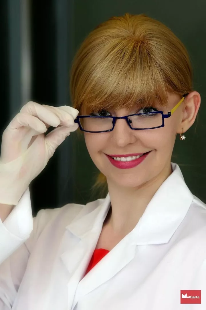 Twarz uśmiechniętej młodej kobiety, która trzyma ręką w ochronnej rękawiczce oprawkę okularów