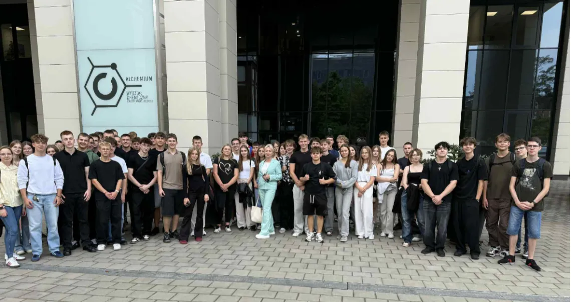 Liczna grupa osób stojaca przed przeszkolnym wejściem do budynku, widocznym w tle, za kolumnami 