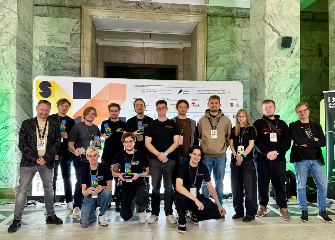 Grupa kilkunastu osób z identyfikatorami na szyi, część trzyma w ręku nagrody, trzy w pierszym rzędzie kucają 