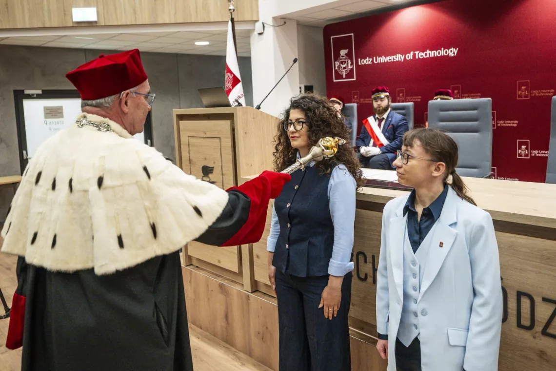 Rektor w oficjalnym stroju dotyka berłem rektorskim ramienia kobiety