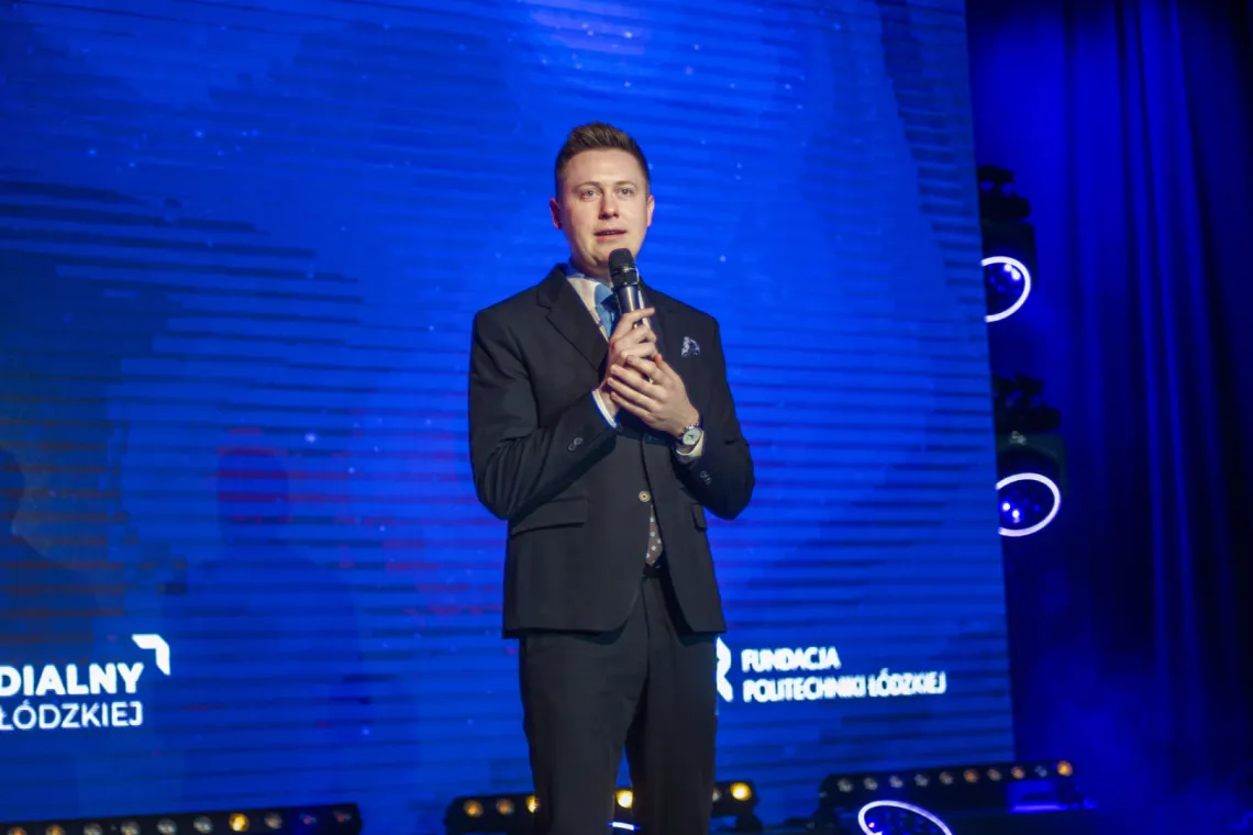 Mężczyzna z mikrofonem w ręku przemawia na tle niebieskiego ekranu