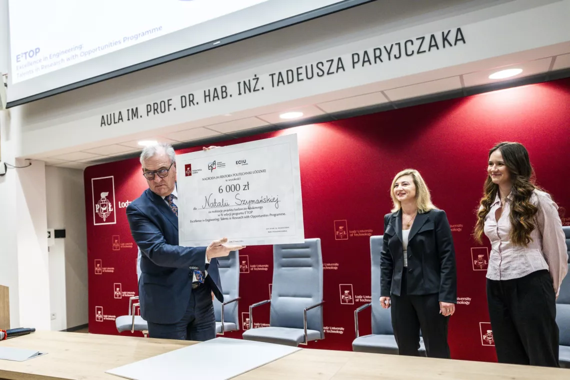 Mężczyzna w garnituzre z czekiem w ręku, obok stoją dwie kobiety