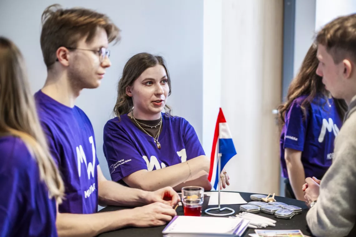 Grupa młodych osób rozmawia, stojąc przy stoliku