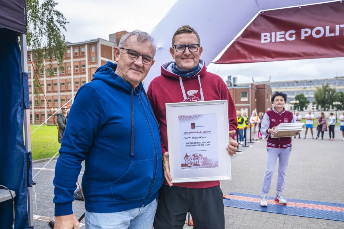 Mężczyzna w granatowej bluzie i mężczyzna w bordowej bluzie z dyplomem w ręku
