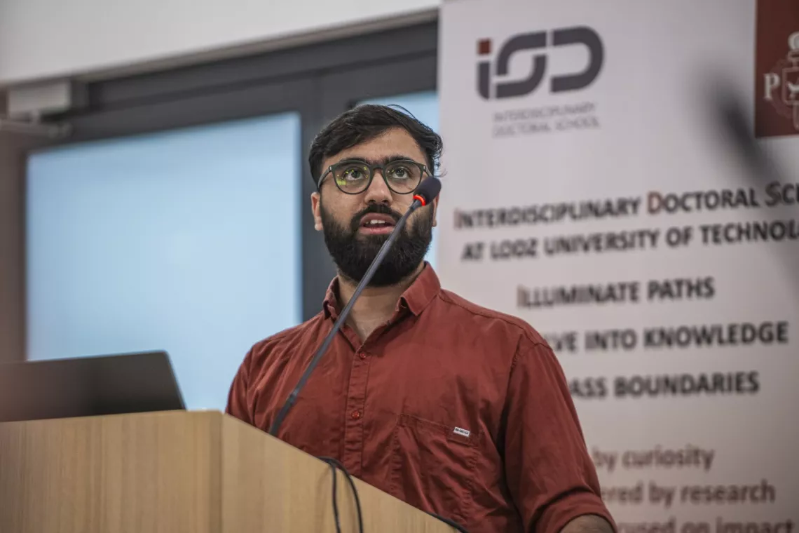 Mężczyzna z wąsami i brodą, w okularach przemawia, stojąc za mównicą