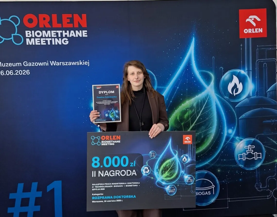 Młoda kobieta trzyma w ręku symboliczny czek i dyplom, z tyłu ścianka z napisem Orlen biomethane meeting