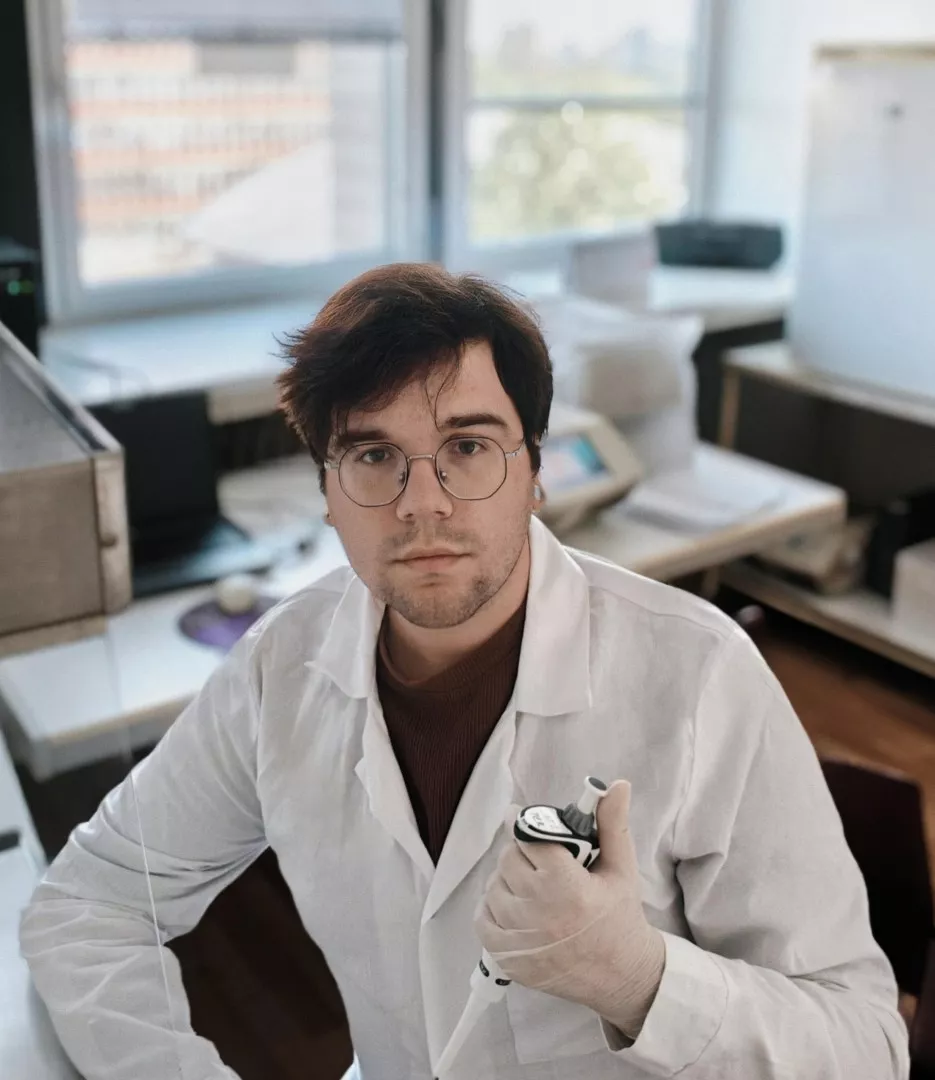 Młody mężczyzna w białym fartuchu siedzi w laboratorium biotechnologicznym trzyma p