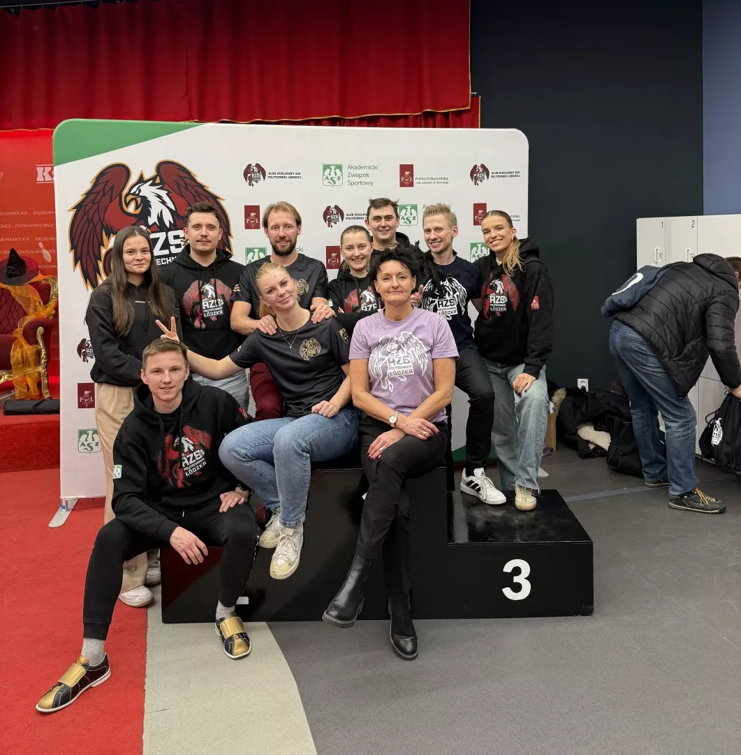 Kilka osób w bluzach AZS stoi wokół podium, kilka na nim przysiadło