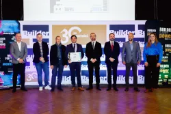 Osiem osób, w tym jedna trzymająca dyplom, stoi na tle promocyjnych, kolorowych ścianek