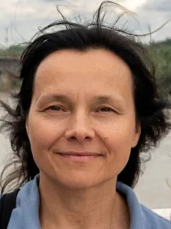 Twarz kobiety uśmiechniętej, ciemne rozwiane włosy, w tle krajobraz naturalny