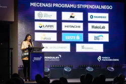 Kobieta przy mówinicy, z tyłu na ekranie wyświetlają się logotypy 11 firm