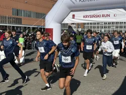 Młodzi ludzie biegną w jednakowych podkoszulkach z numerami startowymi po terenie uczelni