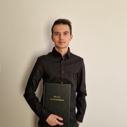 Młody człowiek w ciemnej koszuli stoi i trzyma w ręku egzemplarz wydrukowanej pracy dyplomowej z napisem "praca inżynierska"