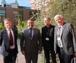 Czterech mężczyzn w garniturach stoi przed budynkiem otoczonym zielenią 