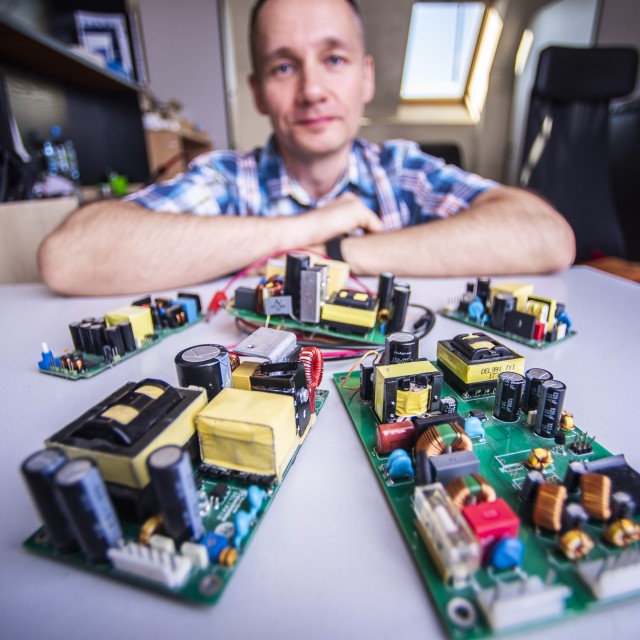 Osobę oparta o stół, na którym jest kilka płytek elektronicznych.