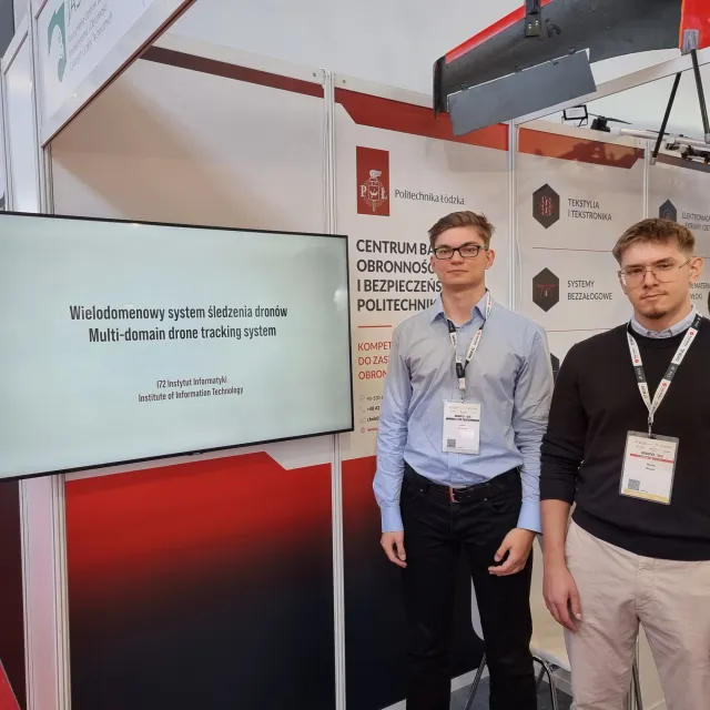 Dwóch młodych mężczyzn na stoisku PŁ, na którym stoi ekran wyświtlający tytuł projektu