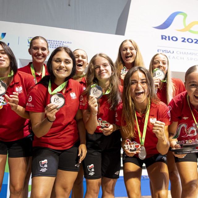 Drużyna sportsmenek prezentuje srebrne medale na tle baneru RIO 2024