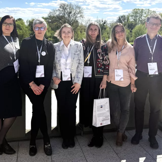 Sześć osób z identyfikatorami konferencyjnymi stoi przy balustradzie drogi prowadzącej nad rzeką