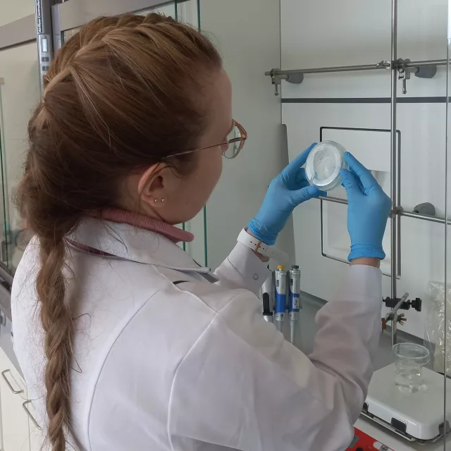 Kobieta w białym fartuchu przygląda się próbce trzymane w rękach