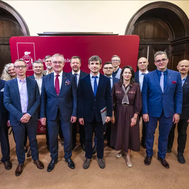 Kilkanaście osób pozuje do zdjęcia na tle baneru z anpisem Politechnika Łódzka